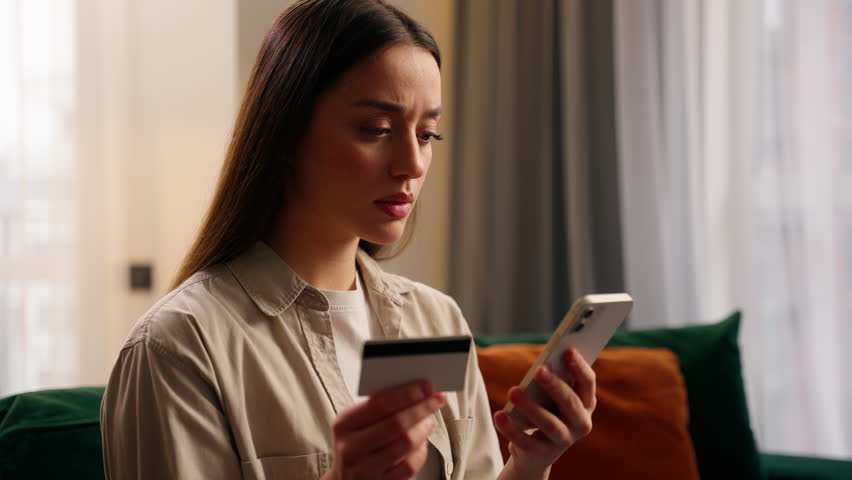 Caucasian woman hold credit card mobile phone trying pay e-bank modern bills app problems funds blocked girl female at home no money insecure payment scam fraud unsuccessful transaction order purchase