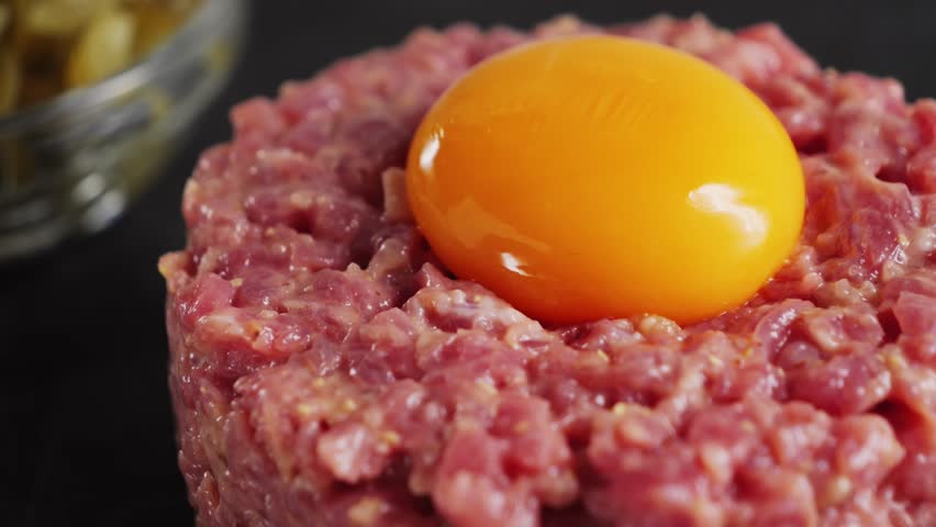 Raw beef tartare with sauce on a black stone platter. Homemade tartare with onions and capers and egg yolk. High quality 4k footage
