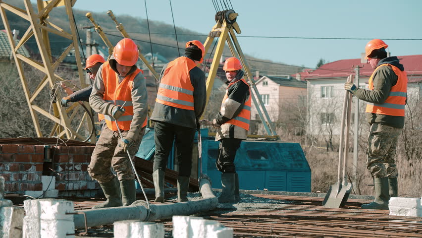 Construction crew pouring concrete on roof slab with crane in background, teamwork under clear blue sky
