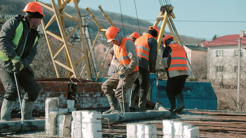 Construction crew pouring concrete on roof slab with crane in background, teamwork under clear blue sky