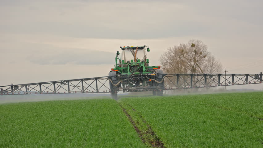 Self-propelled sprayer moving forward across crop field, Agricultural machinery spraying fertilizer over young green plants