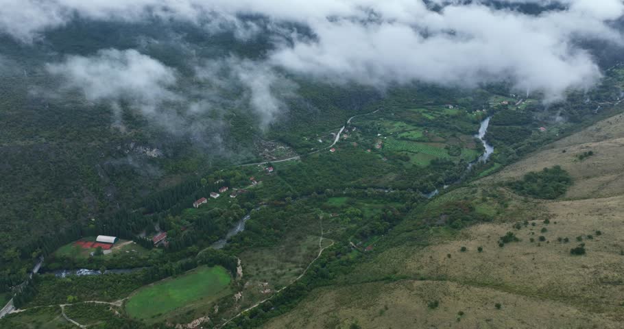HIgh angle view of a town situated in middle of mountains wih clouds on top in Cetinje, Montenegro. Drone shot.