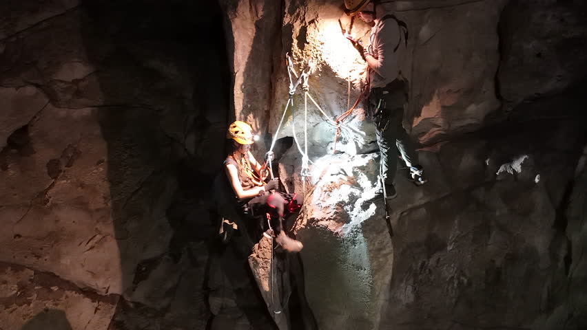 A caver, expertly utilizing Single Rope Technique, is captured mid-descent against the textured rock walls of Anxiety State Cave in Chiang Mai, Thailand. Skill involved in navigating.
