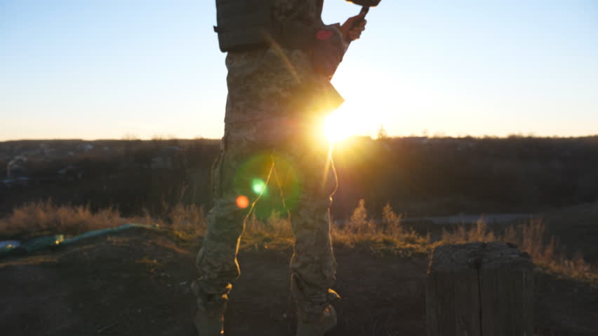 Young man in military uniform waving flag of Ukraine against background of sunset. Male ukrainian army soldier lifting national banner in hill. Victory against russian aggression concept. Rear view