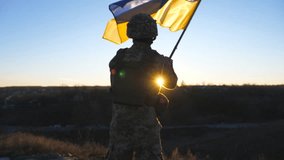 Young man in military uniform waving flag of Ukraine against background of sunset. Male ukrainian army soldier lifting national banner in hill. Victory against russian aggression concept. Rear view - Powered by Shutterstock - Get 15% off with code: PIKWIZARD15