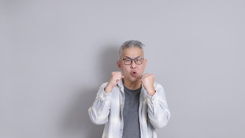 The senior East Asian man, wearing a white plaid-patterned shirt, is standing against a grey background.
