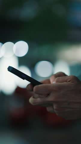 Cropped palms of anonymous human holding modern smartphone and dialing phone number on blurred background. Person moving fingers while interacting with electronic gadget outdoors. Vertical video