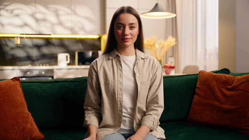 Happy Caucasian woman girl female user showing smartphone mobile phone with green screen relaxing on sofa living room home color chroma key template layout for advertising smiling looking camera app