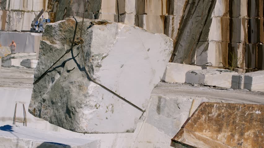 Massive white marble block loading into dump truck, suspended by heavy industrial crane during extraction process