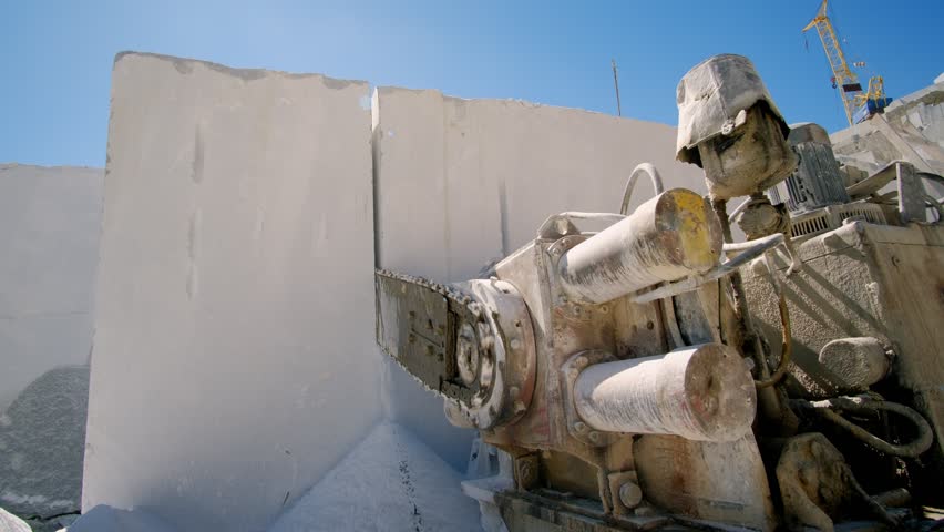 Powerful chain saw cutting white marble block with at industrial marble quarry during stone extraction