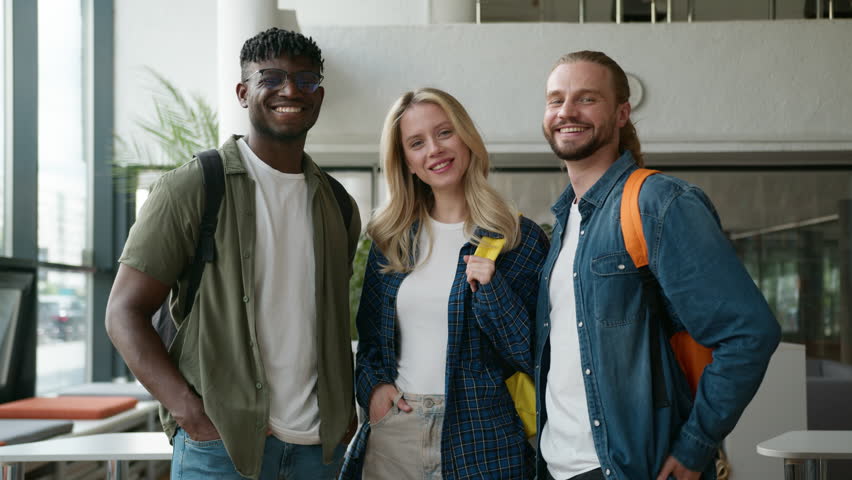 Group of diverse college friends standing together in university hallway smiling at camera cheerful students posing multicultural friendship Caucasian woman girl with African men guys in high school