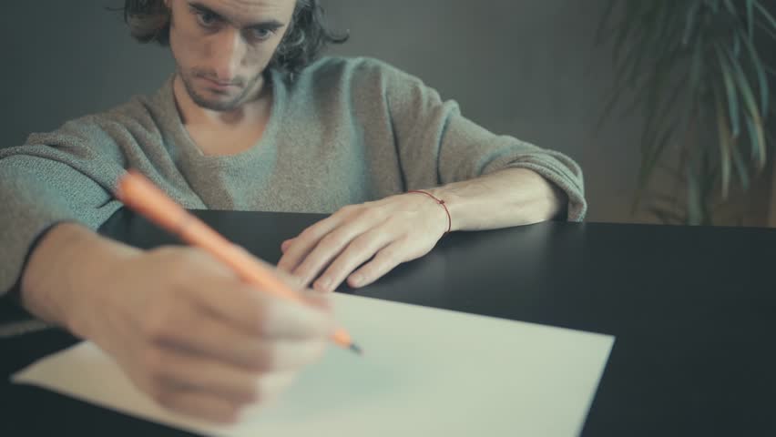 Contemplative Male Artist in Cozy Sweater Drawing with Orange Pencil at Desk, Soft Lighting and Earth Tone Setting, Close-Up Focus on Creative Process