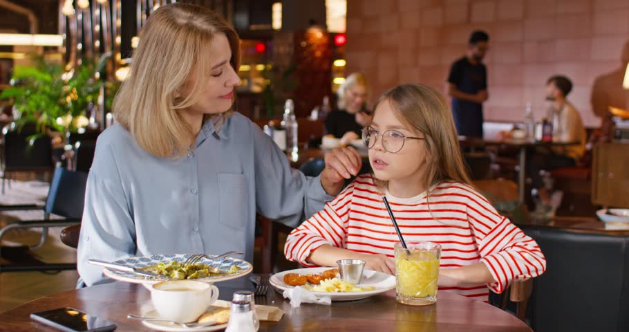 Girl spending time with mother. Mother communicating with daughter. Girl eating french fries with juice at cafe. Childhood and motherhood. Happy mother and daughter enjoying meals and beverage.
