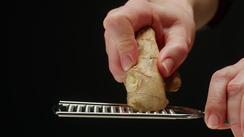 Woman grating ginger on black background, grater with ginger for healthy tea lemonade. 