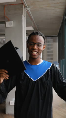Joyful African American student in graduation gown holds diploma and raises arm in celebration