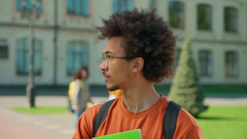 Portrait young male student man African American guy serious calm confident face wearing glasses looking at camera outdoors near university campus outside school college modern educational knowledge