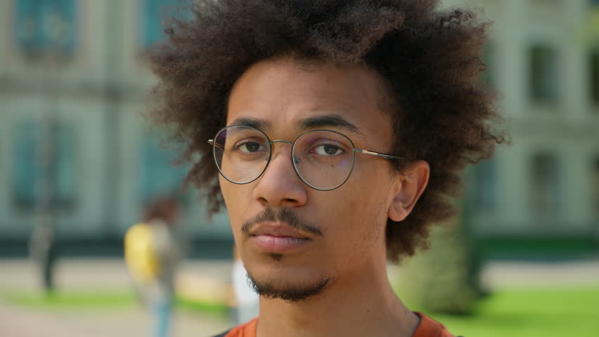 Portrait young male student man African American guy serious calm confident face wearing glasses looking at camera outdoors near university campus outside school college modern educational knowledge