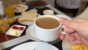 good coffee in a white cup for breakfast, a woman's hand holds it, side view, in the background lie toasts with butter, jam and other table setting, buffet hotel all inclusive, caffeine enjoyment - Powered by Shutterstock - Get 15% off with code: PIKWIZARD15