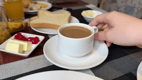 good coffee in a white cup for breakfast, a woman's hand holds it, side view, in the background lie toasts with butter, jam and other table setting, buffet hotel all inclusive, caffeine enjoyment - Powered by Shutterstock - Get 15% off with code: PIKWIZARD15