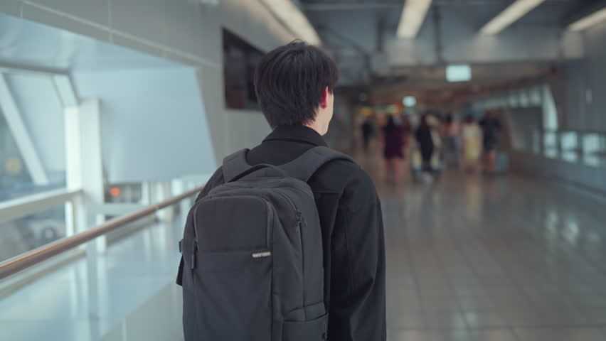Rear view - Male traveler walking with luggage at the modern airport terminal, man on way to flight boarding gate, Ready for travel or vacation journey.