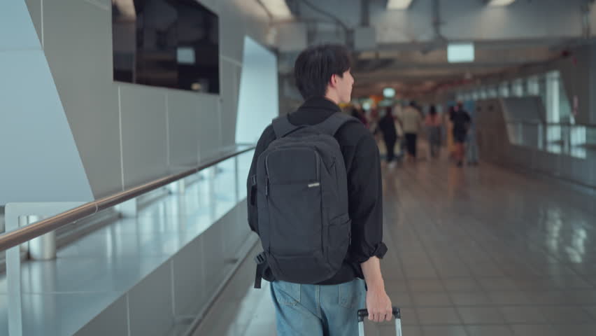 Rear view - Male traveler walking with luggage at the modern airport terminal, man on way to flight boarding gate, Ready for travel or vacation journey.