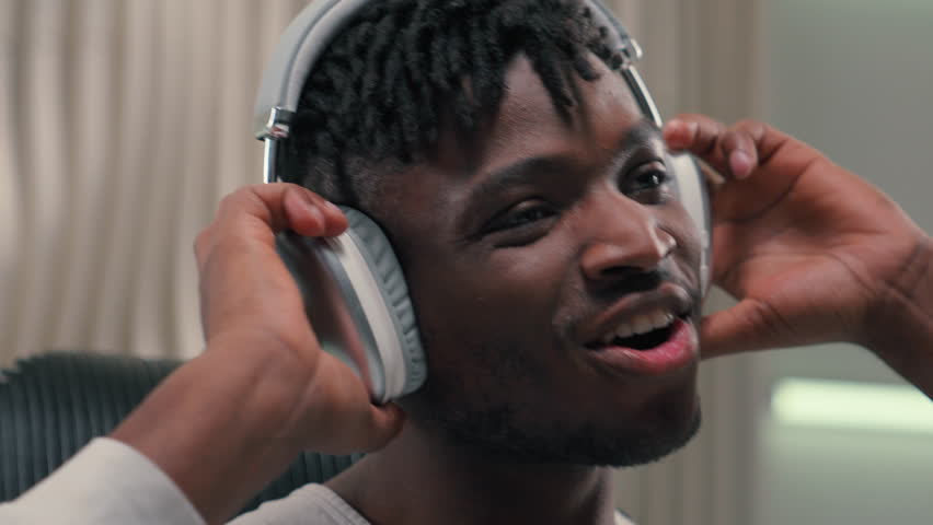 Portrait emotional happy carefree satisfied relaxed ethnic man African American male guy indoors in white futuristic studio relaxing freedom smiling wearing headphones listening energetic music dance