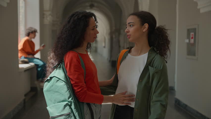 Hispanic sad upset frustrated woman student walking in college university corridor hall girl female friend meeting talking supporting calming girls students hugging friendship help care problem school