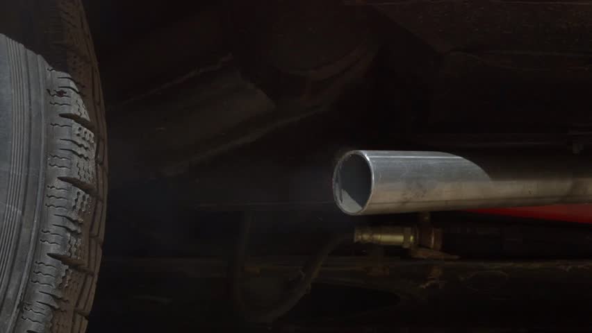 Slow motion closeup of thick white smoke billowing from a car exhaust pipe, releasing harmful carbon monoxide. The vehicle emits fumes on the road, highlighting the concept of air pollution in traffic