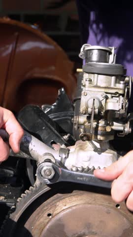 Vertical Mechanic works carefully on a vintage motor part using tools in a bright garage, showcasing the precision and attention required for detailed car repairs in a Spanish workshop.