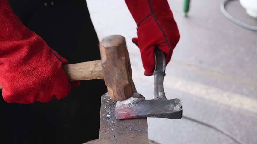 Skilled artisan shapes glowing axe making on an anvil while wearing protective gloves.