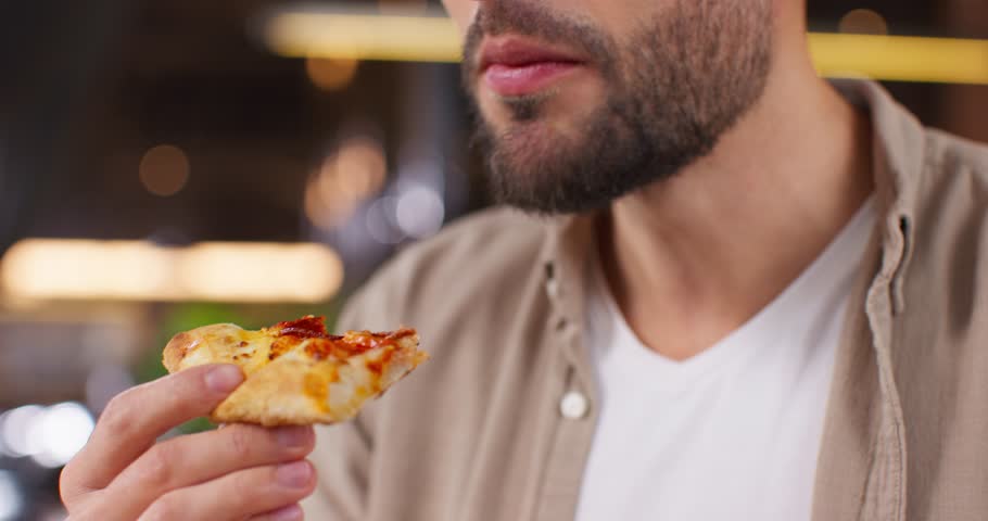 Close up shot of caucasian man eating piece of pizza. Bearded man tasting fragrant pizza. Male holding piece of pizza. Close up view of man eating delicious pizza. Portrait of satisfied man.