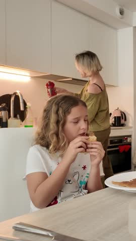 Girl eating breakfast while mother prepares coffee