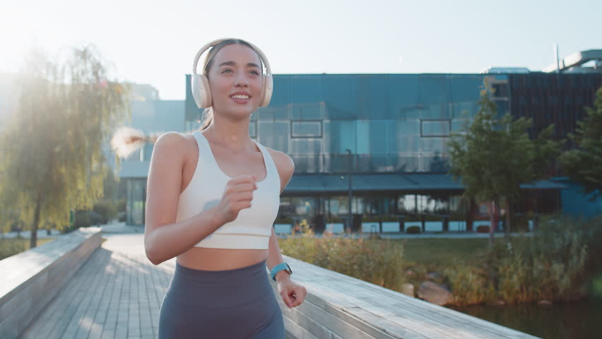 Athletic runner adult girl looks at smartwatch device fitness bracelet checking time, heart rate, pulse, SPO2 on smartwatch on jogging. Young woman listening music working out cardio in city park.