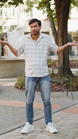 I don't know what to say. Confused young man feeling embarrassed about ambiguous question, having doubts, no idea, being clueless uncertain outdoors. Arabian adult guy standing on urban city street.
