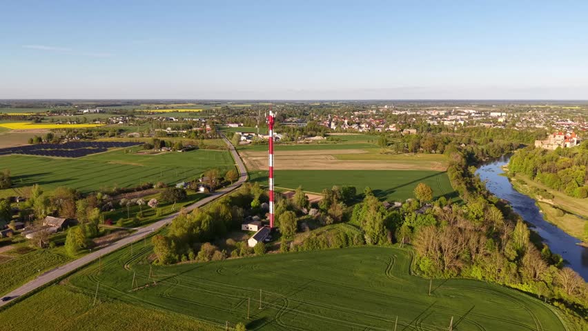 Aerial View of Rural Landscape with Communication Tower and River Drone video showing a red and white communication tower in a green rural landscape.