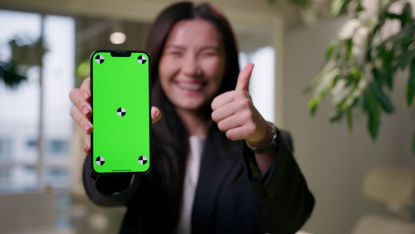 Smiling Asian woman girl Chinese Korean Japanese businesswoman user holding mobile phone chroma key green screen business ads mockup copy space recommend smartphone app online store shopping thumb up