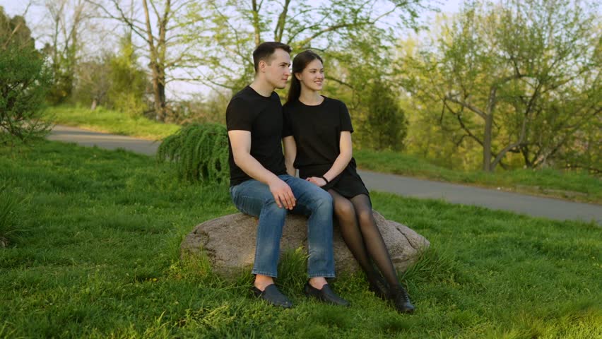 Couple enjoys a serene moment on a rock in a lush green park