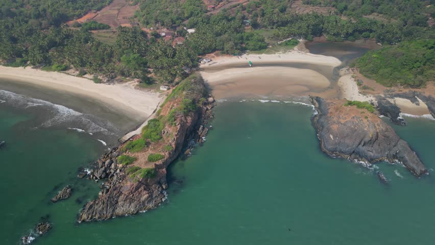 River meets the ocean at low tide in Goa, India. Wide sandbanks, lush greenery, calm waters and a fishing boat form a tranquil coastal view. Tropical light diffuses over the landscape