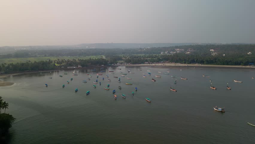 A broad river mouth meets the sea near anchored boats. Fields and forest frame the serene coastline. Coconut palms border a quiet estate and pool. Nearby bay hosts fishing boats under morning light