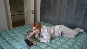 An elderly Caucasian woman in pajamas lies on a bed using a laptop. Conversation on a video link.  - Powered by Shutterstock - Get 15% off with code: PIKWIZARD15