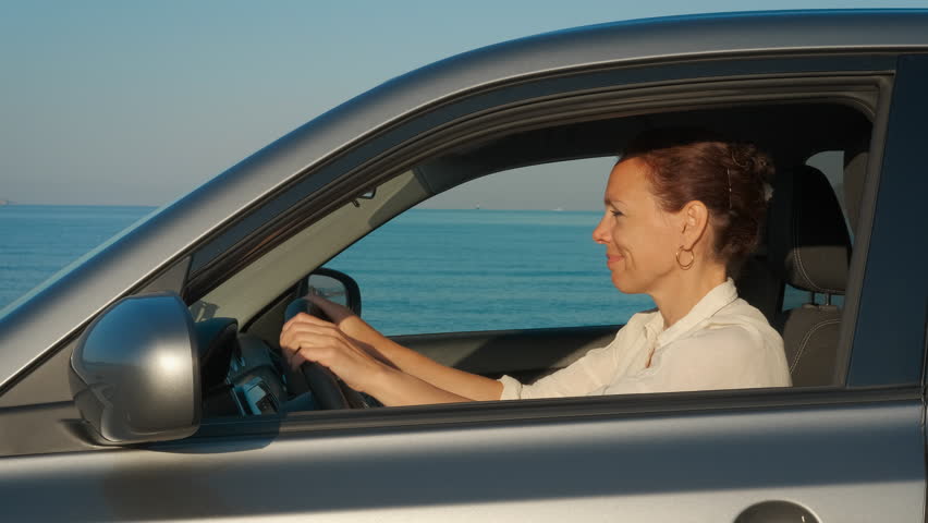 Alone woman driving along sea road. An alone relaxing female driving the car along the beach in the sun light.