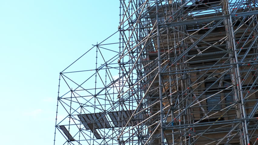 Scaffolding. Workers assembling complex scaffolding structure on a construction site. Crane operating overhead under clear blue sky, enhancing urban development dynamics