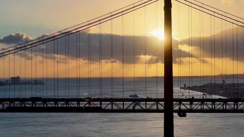 Sunset Skyline Of 25Th April Bridge At Lisbon In District Of Lisbon Portugal. Sunset Cityscape. Cable Bridge Scene. 25Th April Bridge At Lisbon In Portugal. Train In Bridge Landscape. Elevated Road.