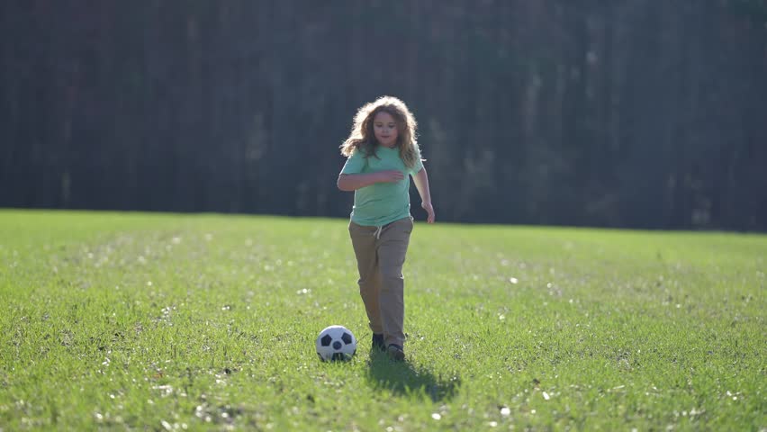 Active child playing football. Kid boy kicking a football on the grass. Kid running with a soccer ball. Playful children enjoying a football game. Kids soccer match. Kid playing football kicking ball.