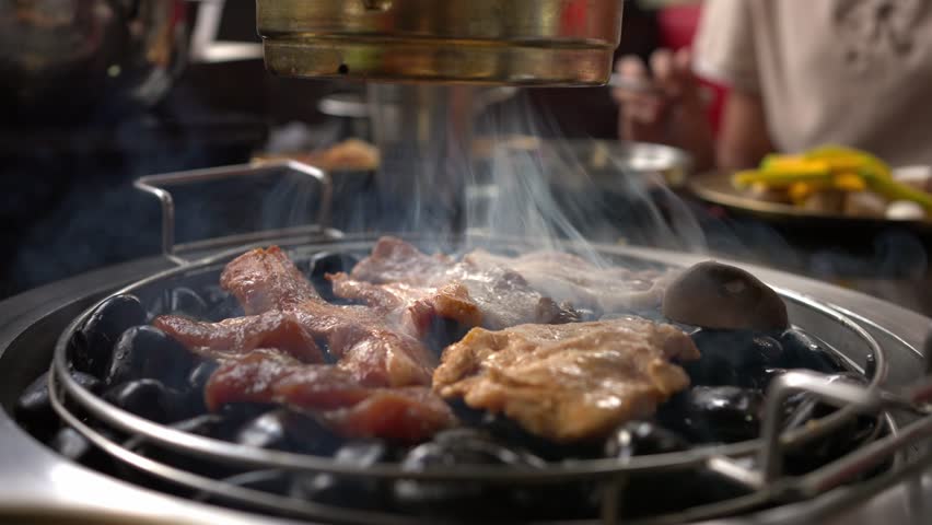 Chef hand cooking smoked grilled pork on iron grill pan in Korean BBQ in restaurant. Traditional Korea style food barbecue pork belly steak on charcoal grill