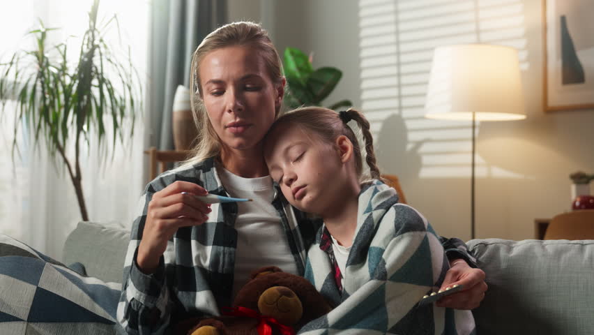 Family at home Caucasian mother woman caring hugging ill sick girl child daughter coughing fever mom holding thermometer high temperature check kid drinking remedy medication health problem medicine
