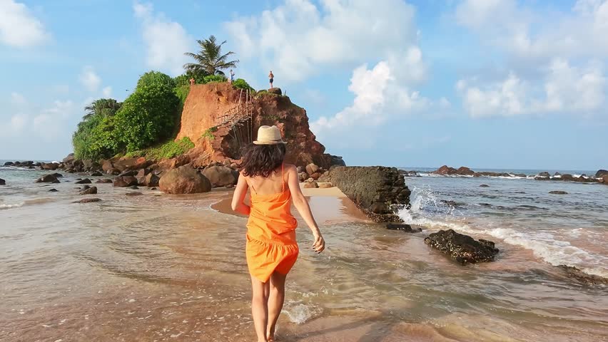 Excited Tourist smiley Woman Running Joyfully in Scenic Sri Lanka sunny beach.Parrot island popular landmark attraction. Mirissa coastline. Sri lanka travel sightseeing concept.