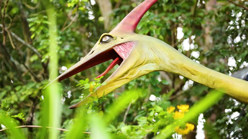 A vibrant Pteranodon sculpture stands among dense foliage and flowers, captured in bright daylight at a dinosaur park