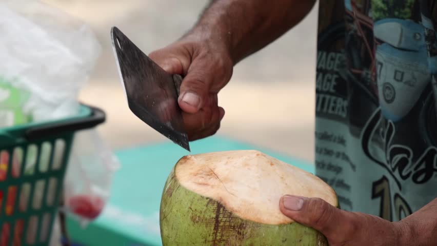 A vendor expertly slices a coconut using a machete, showcasing skillful hand movements.