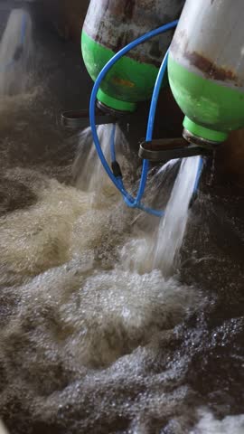Rusted green and silver gas cylinders expelling water in a testing or maintenance station with metal grating below to drain liquid efficiently